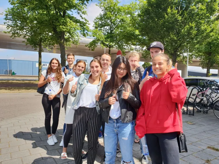 Groep cursisten van de theoriedagcursus poseert lachend buiten, met duimen omhoog.