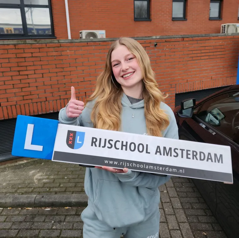 Geslaagde leerling houdt lachend het dakbord van Rijschool Amsterdam vast, met de duim omhoog.