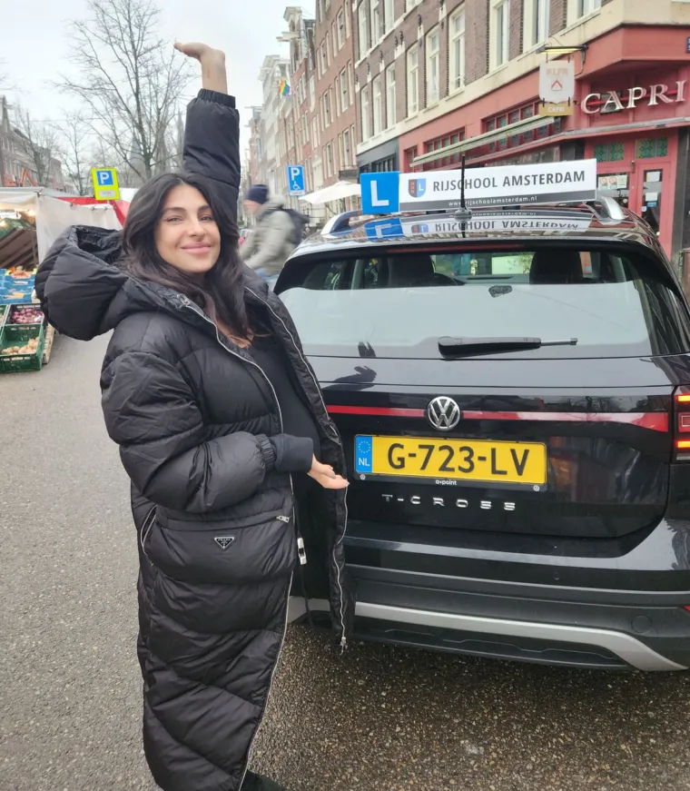 Geslaagde leerling naast de zwarte T-Cross van Rijschool Amsterdam in een Amsterdamse marktstraat.